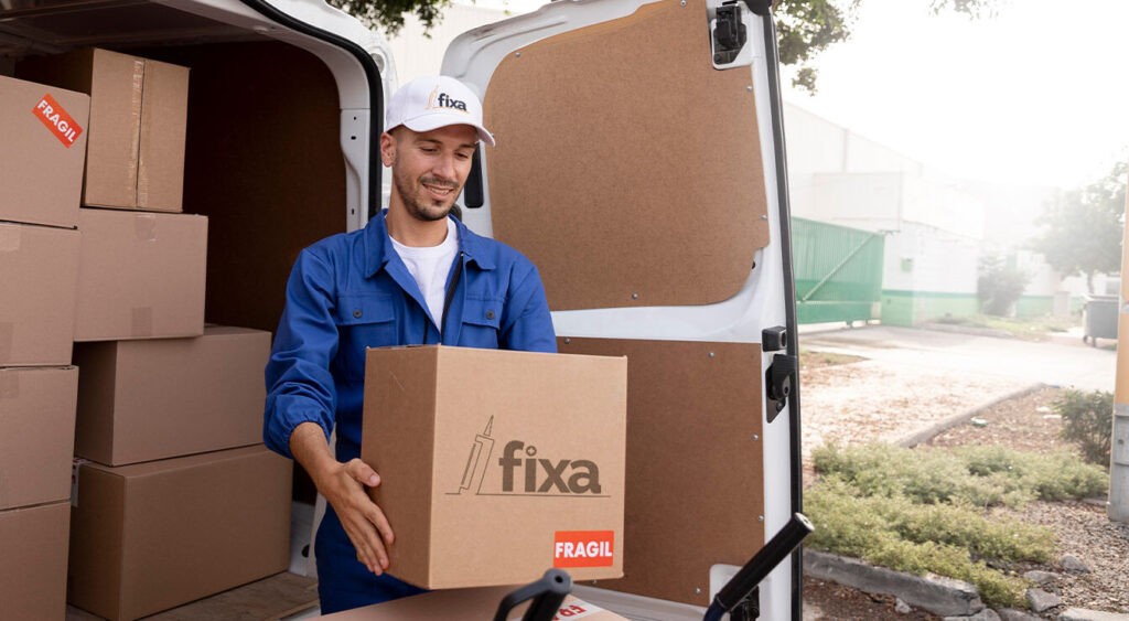 Homem segurando caixa da Fixa e colocando em um carrinho, com o caminhão de entrega no fundo